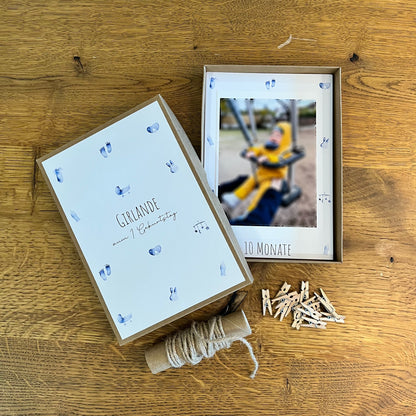 Dekorative Fotogirlande zum ersten Geburtstag mit blauen Babymotiven, Klammern, Juteschnur, Box und Platz für Babyfotos.