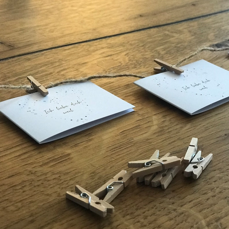 „Ich liebe dich, weil …“-Kärtchen mit Herzmotiv aufgehängt mit Schnur und Klammern.